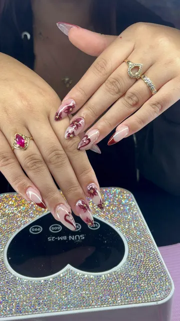 Close-up of almond nails with burgundy hand-painted flowers, gold studs and red French tips